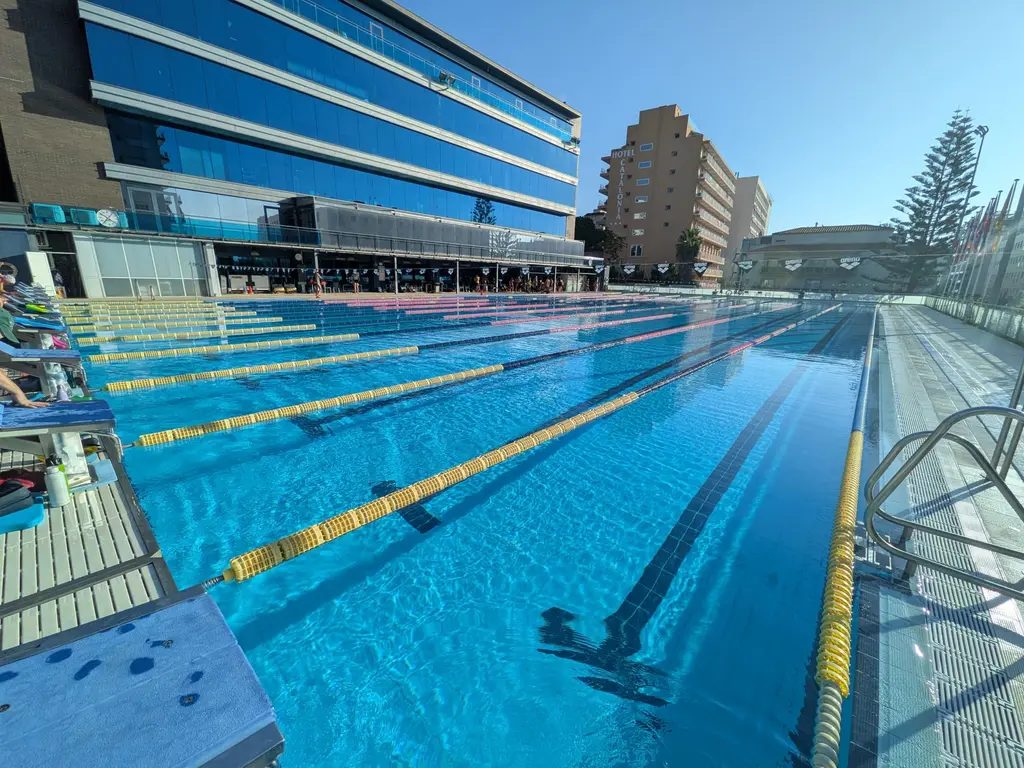 A fifty metre pool under hard mid morning sun, lane ropes strung out, nobody swimming.