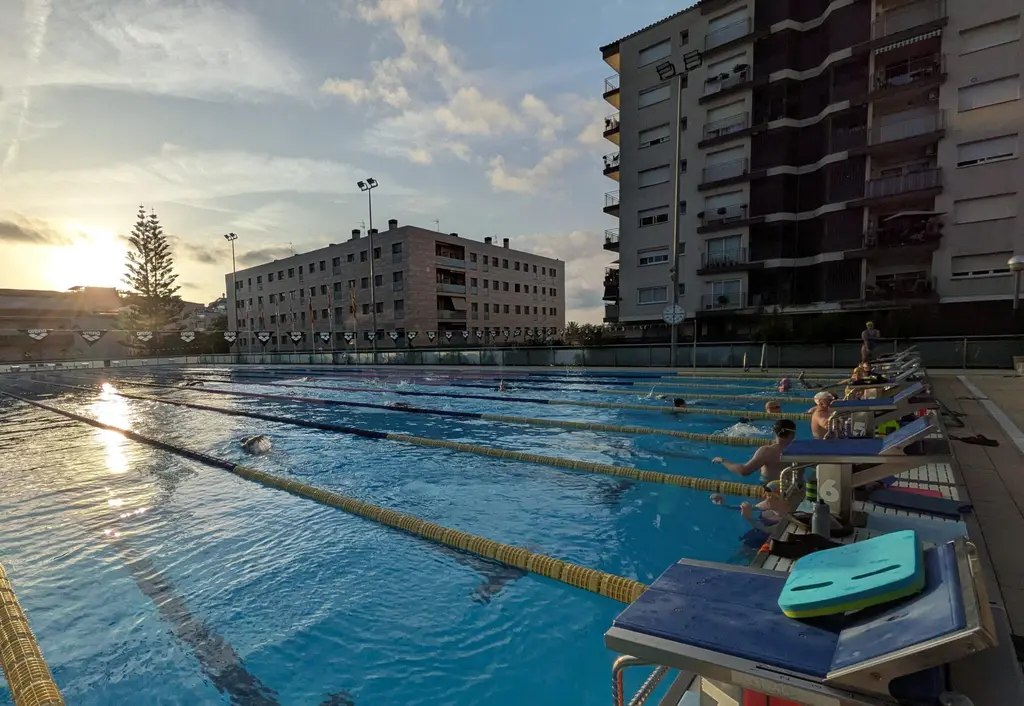 Swimmers moving down several lanes in low evening sun, kickboards stacked on the starting blocks.