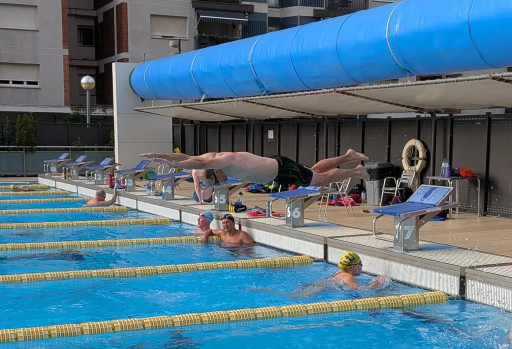 A swimmer in full flight off a starting block, body flat and horizontal above the water.