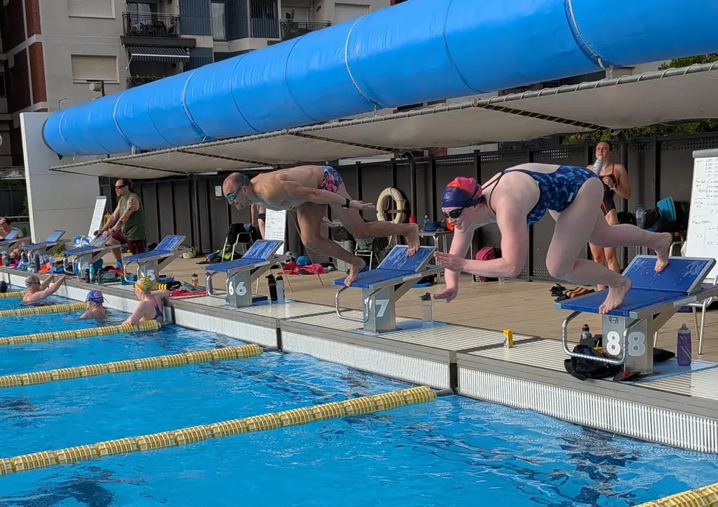 The same two swimmers a moment later, both grinning as they leave the blocks.