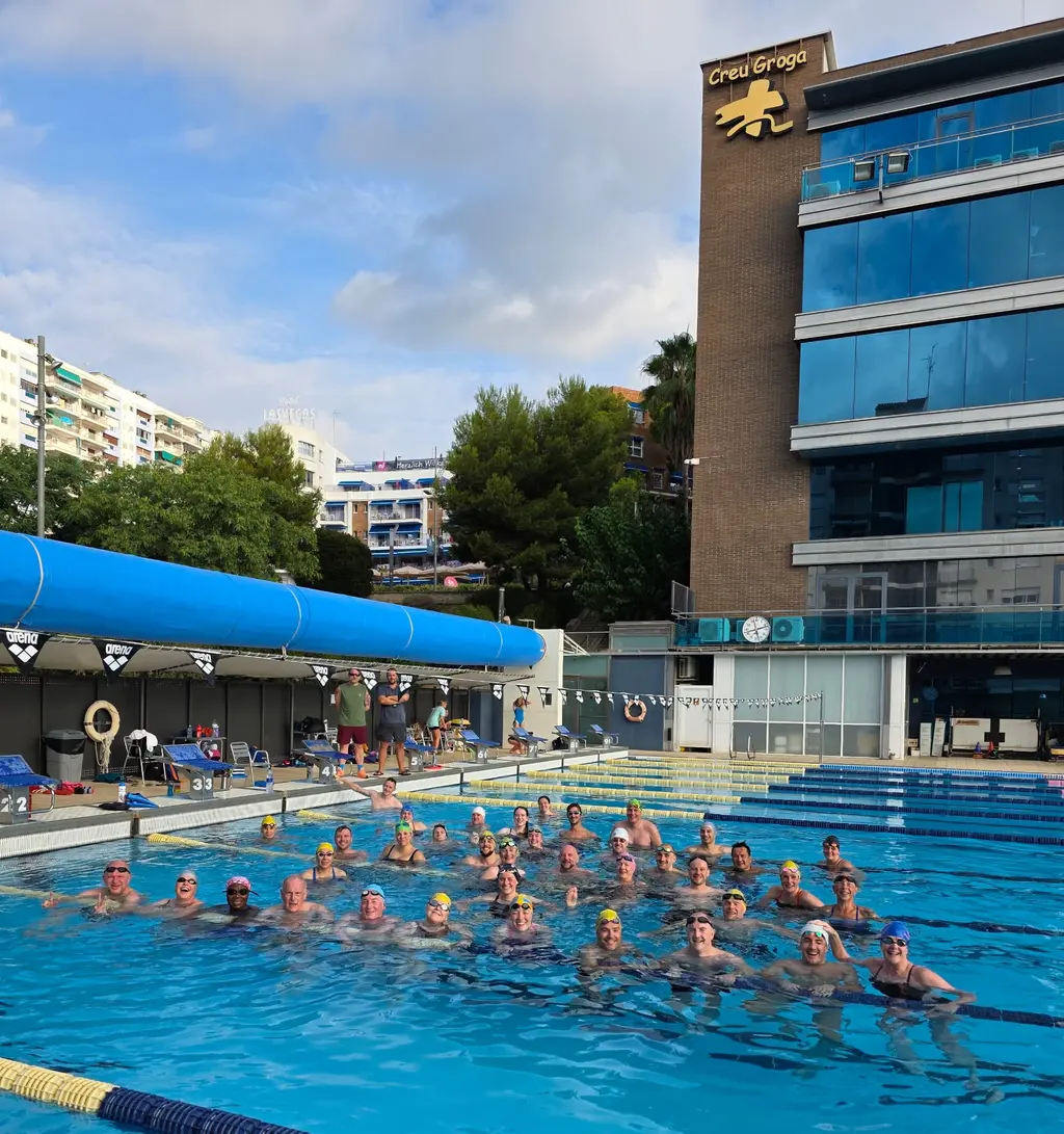 The whole squad gathered in the shallow end of the pool, most of them in caps and goggles, looking up at the camera.