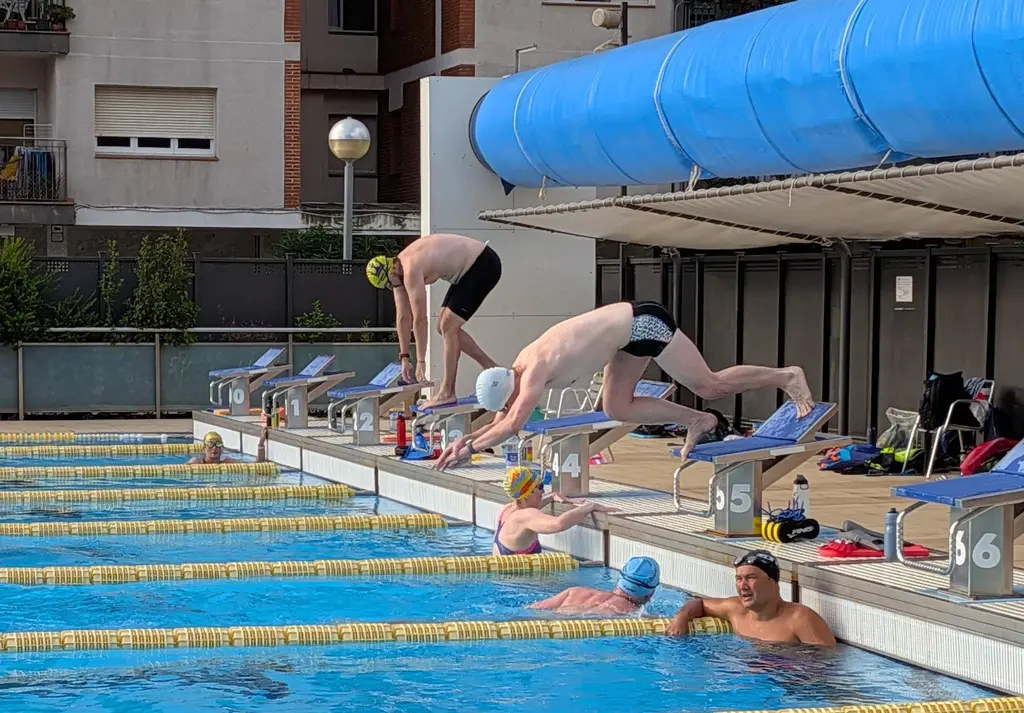 Two swimmers leaving the blocks mid set while others wait in the lane below.